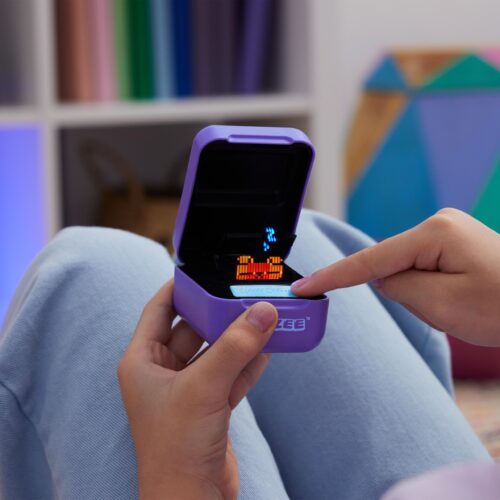 Nahaufnahme einer Hand, die das Bitzee Spielgerät hält, ein pädagogisches Elektronikspielzeug mit farbenfrohen Pixeln auf dem Bildschirm.